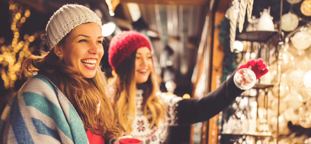 Women outdoors shopping at an oudoor holiday shop. looking at glass decorations. They are wearing hats, coats, gloves indicating winter and cold.